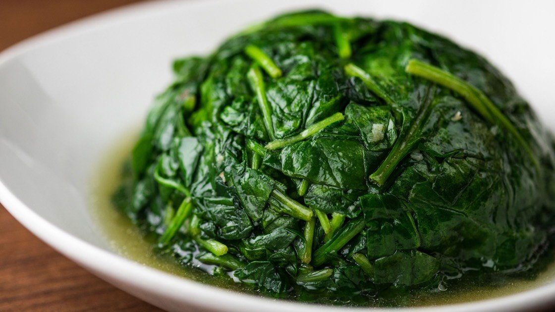 Round of sauteed Spinach with Garlic in a white dish, close up