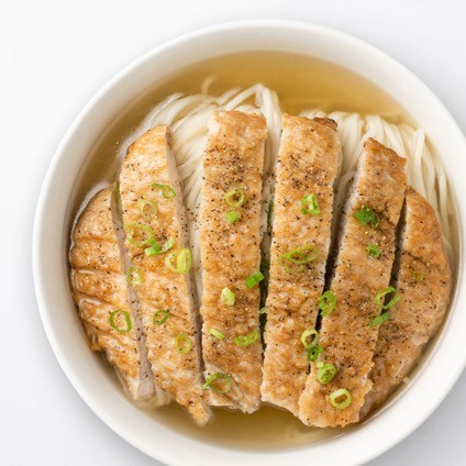 Sliced pork chop on top of  noodle soup in a white bowl