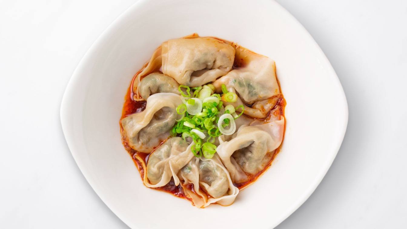 Vegetable & Kurobuta Pork Wontons with Spicy Sauce in a white bowl