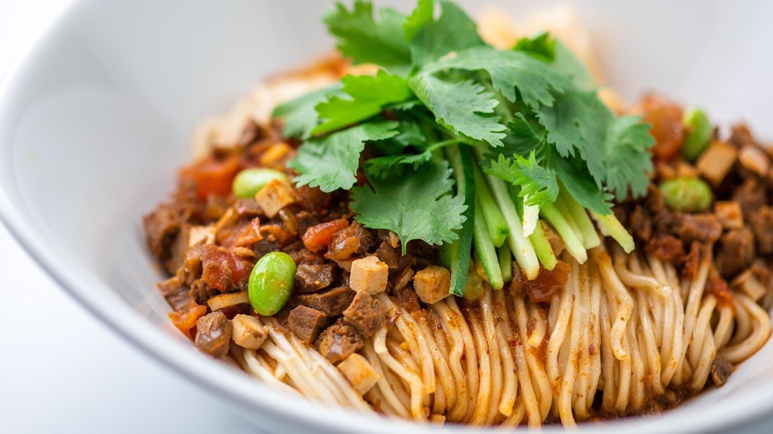 Noodles with Diced Beef & Szechuan Peppers in a white bowl, close up