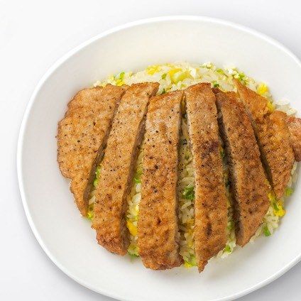 Sliced pork chop over fried rice on a white plate
