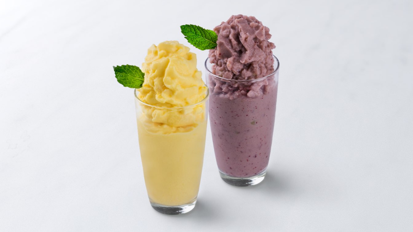Two fruit smoothies side-by-side in glasses topped with a sprigs of mint.